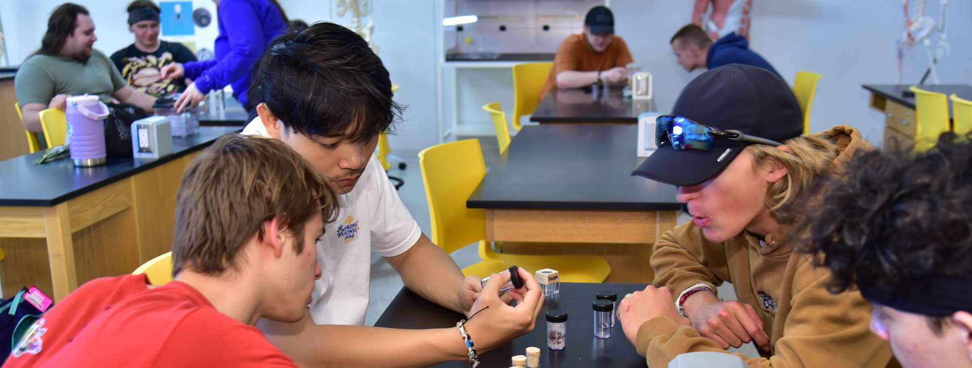 Students working in a science lab, holding and viewing samples in small vials